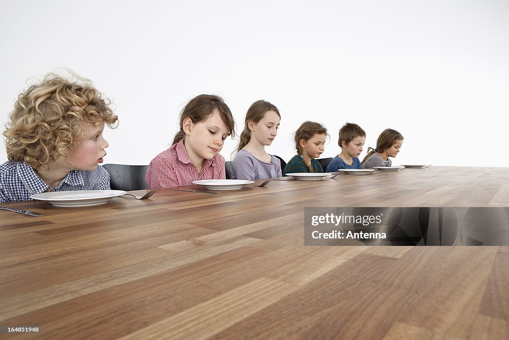 Six sad kids looking down longingly at their empty plates