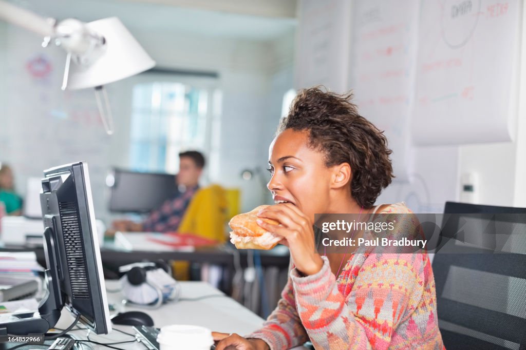 Businesswoman eating burger at desk
