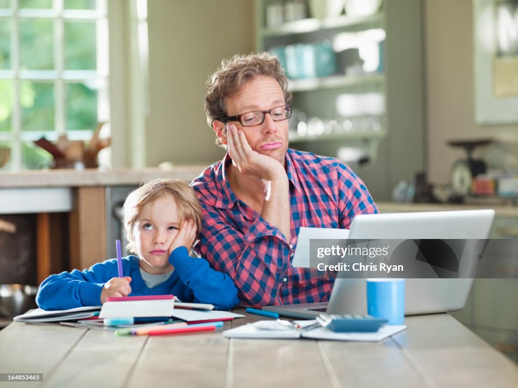 Bored father and son working at table