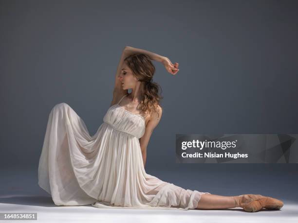 ballet dancer sitting with leg stretched out in studio wearing beautiful dress - performing arts center stock pictures, royalty-free photos & images