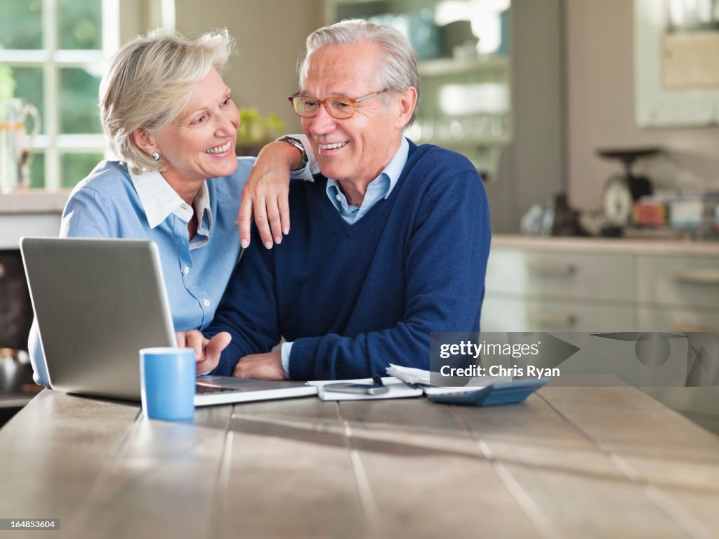 Couple using laptop at kitchen table