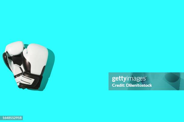 black and white boxing gloves, on the left side, on a turquoise background. concept of boxing, sport, combat, fight, training, effort, strength, changeability and sportsmanship. - boxing glove coloured background stock pictures, royalty-free photos & images