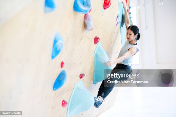 sport climbing can helps enhanced patience, perseverance, courage, trust, will power, and self-control. a female climber to climbing and griping on an artificial wall to develop her body strength in an indoor rock climbing gym. - personalized photos et images de collection