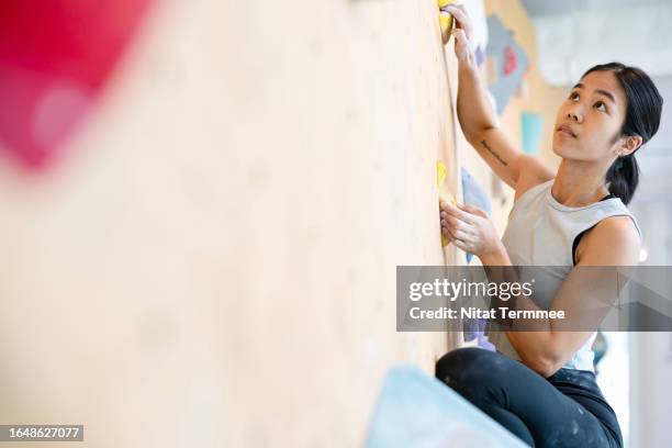 rock and wall climbing can help you with problem-solving and increases strength and grip. side view of a female japanese climber climbing up on a bouldering wall at a rock climbing gym. - chalk wall stock pictures, royalty-free photos & images