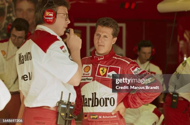 German racing driver Michael Schumacher, wearing red coveralls, in conversation with a team official ahead of the Hungarian Grand Prix, held at the...