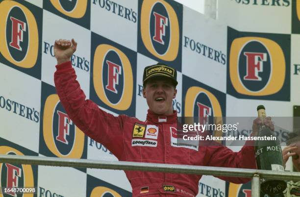 German racing driver Michael Schumacher, wearing a black Goodyear baseball cap and red coveralls, holding a bottle of champagne on the winners'...
