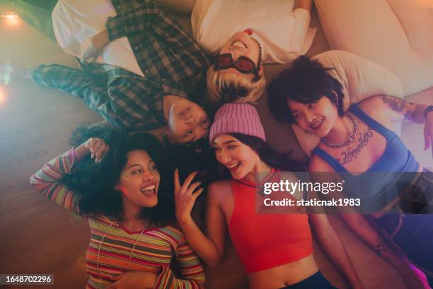 multiethnic friends lying on floor together looking happily at the beautiful lights in the room. - friends girl stock pictures, royalty-free photos & images