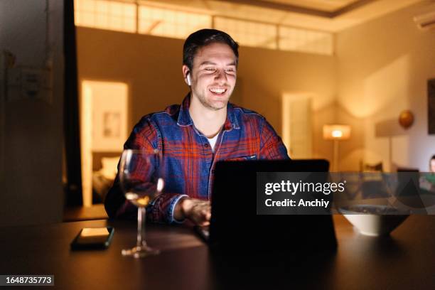 man talking with someone on a video call at home - online happy hour stock pictures, royalty-free photos & images