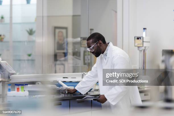 male chemistry student reads his lab report while working in the laboratory - clean suit stock pictures, royalty-free photos & images