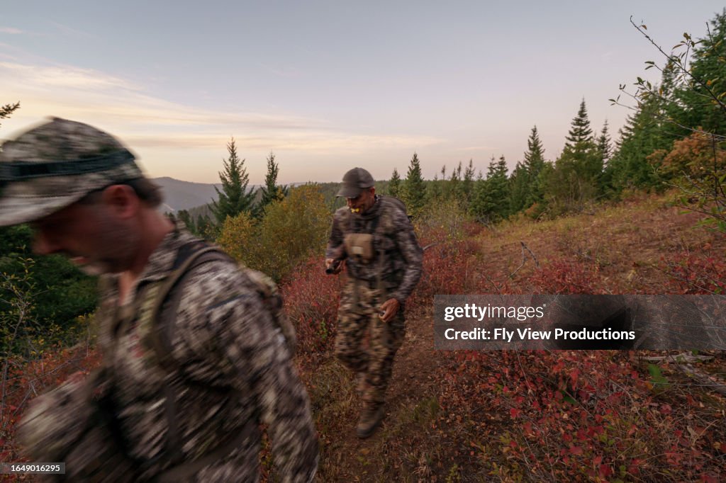 Zwei Jäger wandern im Morgengrauen auf einem bergigen Pfad