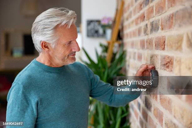 senior man adjusting the temperature using a smart thermostat - thermostat stock pictures, royalty-free photos & images
