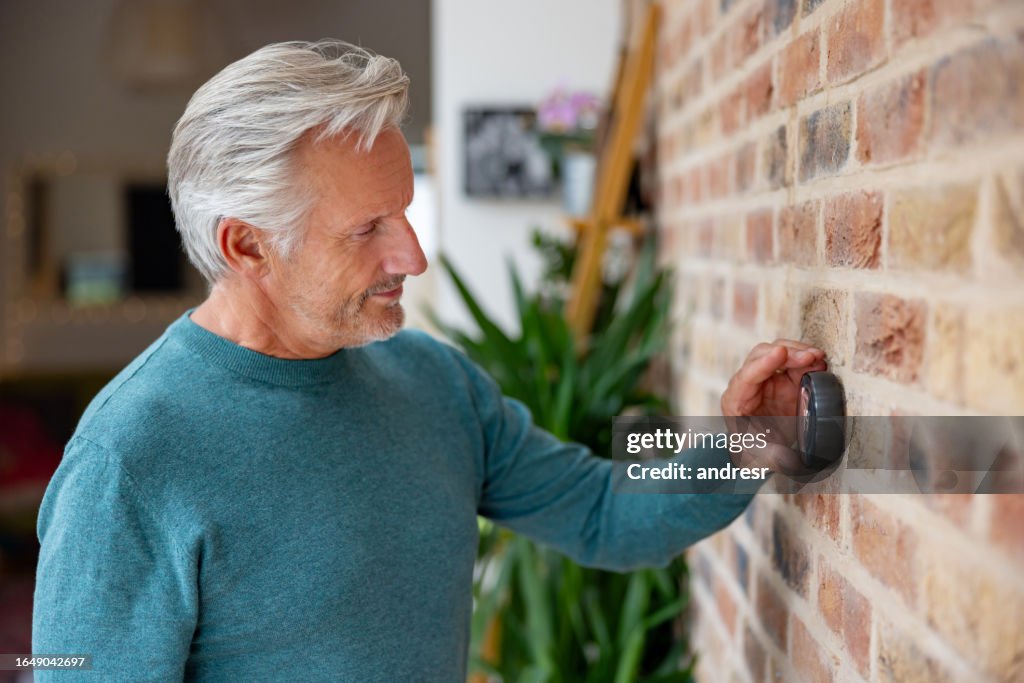 Senior man adjusting the temperature using a smart thermostat