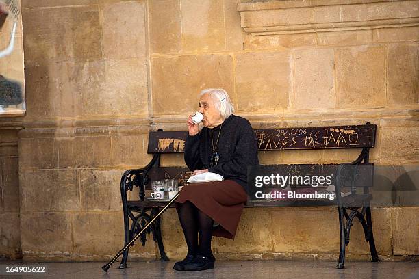 An elderly woman sits and drinks coffee on a bench in a churchyard in Nicosia, Cyprus, on Friday, March 29, 2013. Cypriots face a second day of bank...