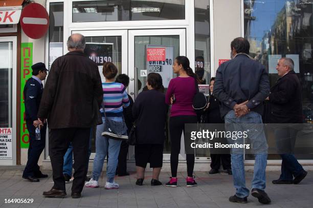 Police officer, left, talks with customers as they queue outside a branch of Cyprus Popular Bank Pcl, also known as Laiki Bank, in Nicosia, Cyprus,...