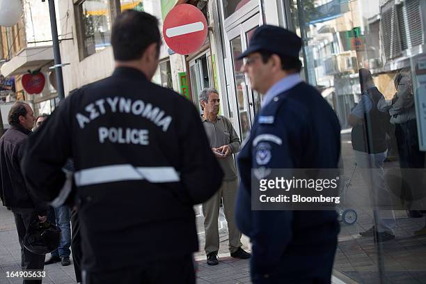 Police officers stand guard as customers wait to be allowed inside a branch of a Cyprus Popular Bank Pcl, also known as Laiki Bank in Nicosia,...