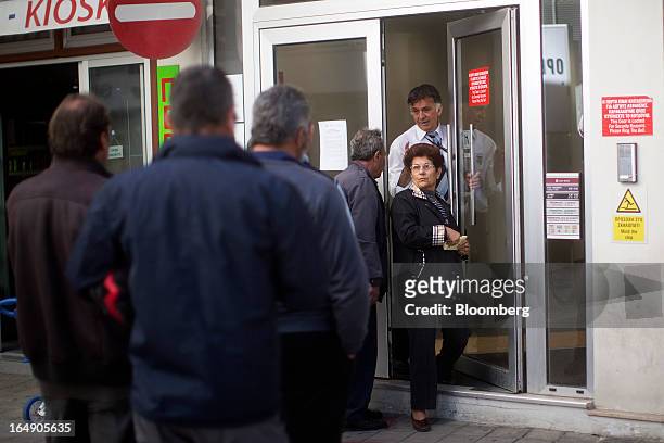 Security guard lets a customer exit a branch of a Cyprus Popular Bank Pcl, also known as Laiki Bank, as other customers wait their turn to enter, in...