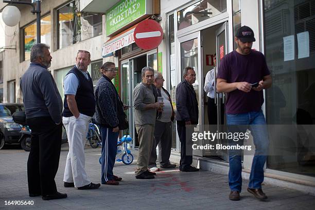 Security guard stands at the door of a Cyprus Popular Bank Pcl, also known as Laiki Bank, as customers wait their turn to enter, in Nicosia, Cyprus,...
