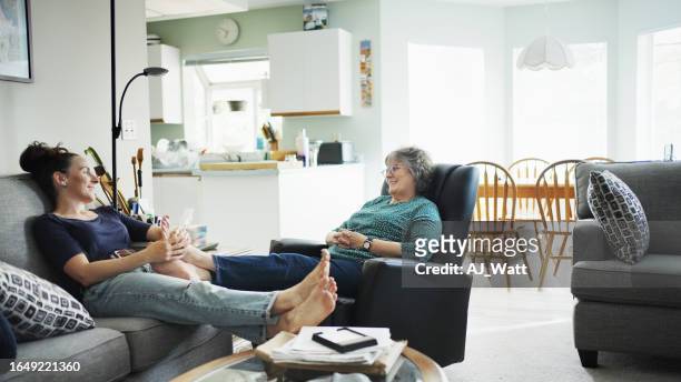 young woman giving her smiling mom a foot massage during a visit - woman foot massage stock pictures, royalty-free photos & images