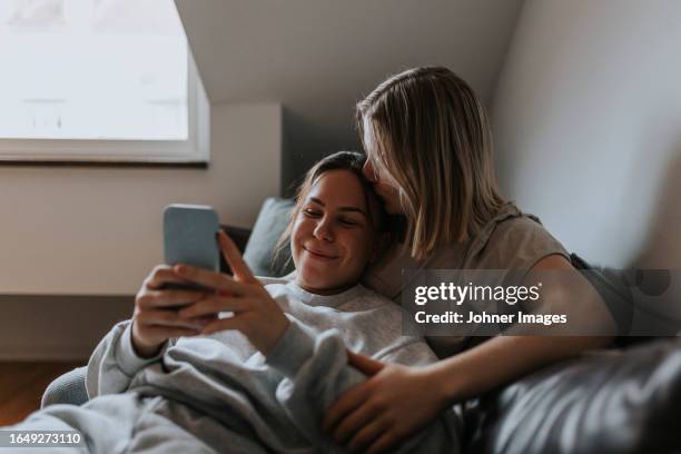 female couple relaxing together on sofa and looking at cell phone - lgbtq  and female domestic life fotografías e imágenes de stock