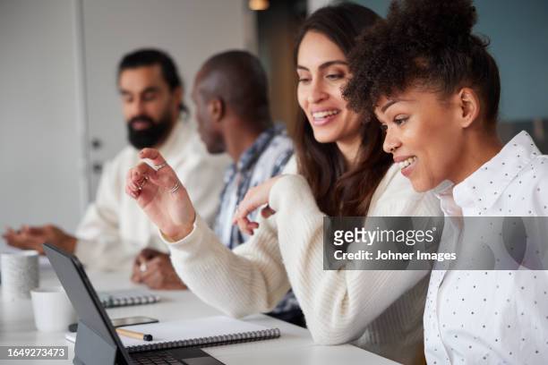 smiling women sitting at business meeting and looking at laptop - gemengde afkomst stockfoto's en -beelden