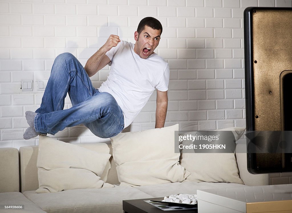 Young adult man watching football on television: Goal!