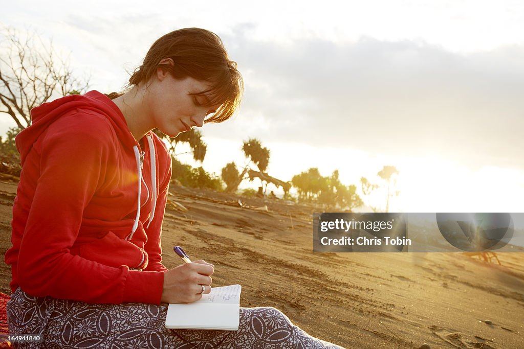 Young woman writing in journal on the beach
