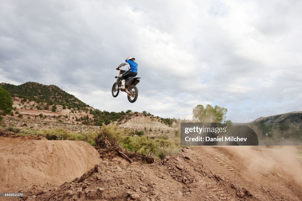 Man takin goff a dirt jump, on his motocross bike.