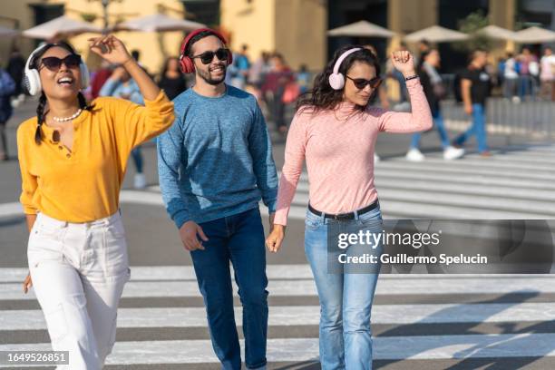 three friends walking and dancing while listening to music on their headphones - just dance 3 stock pictures, royalty-free photos & images