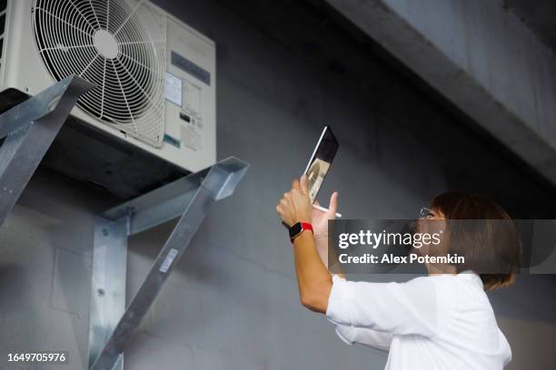 air conditioning leakage fixation. female claim agent with digital tablet take photos of split system modules from different angles indoors - heat pump stock pictures, royalty-free photos & images