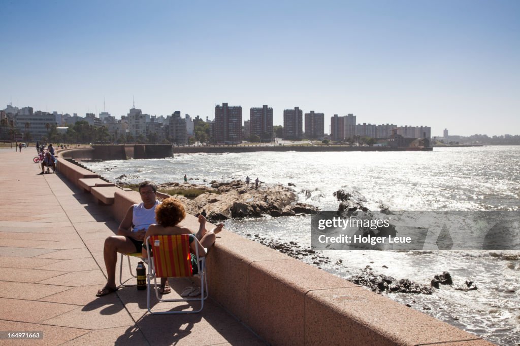 People relax on seawall and drink mate