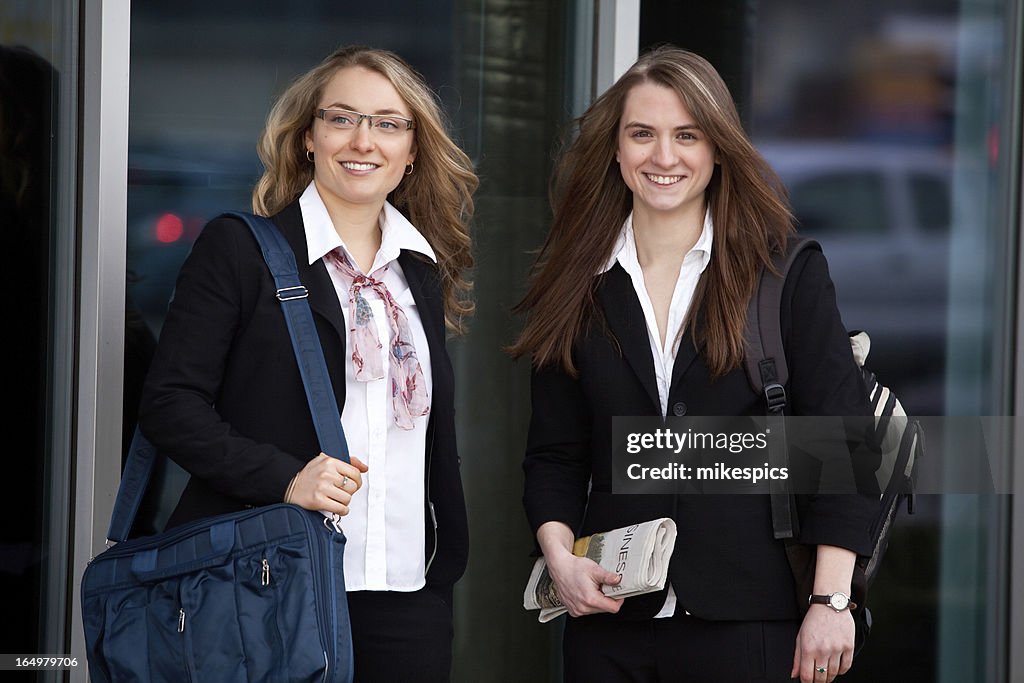 Two young professional women outside a glass building.