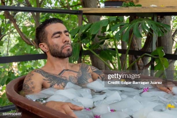 a man inside a tub with ice doing cryotherapy and meditating - eis baden stock-fotos und bilder