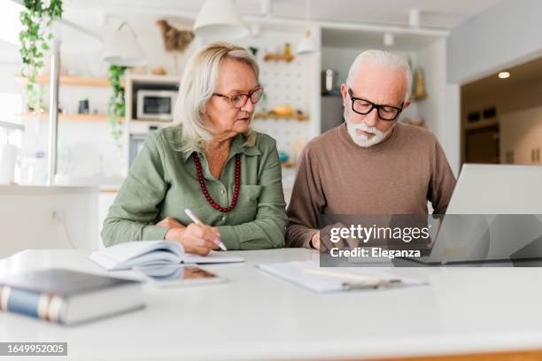 senior couple using laptop while planning their home budget, - pensão documento bancário imagens e fotografias de stock