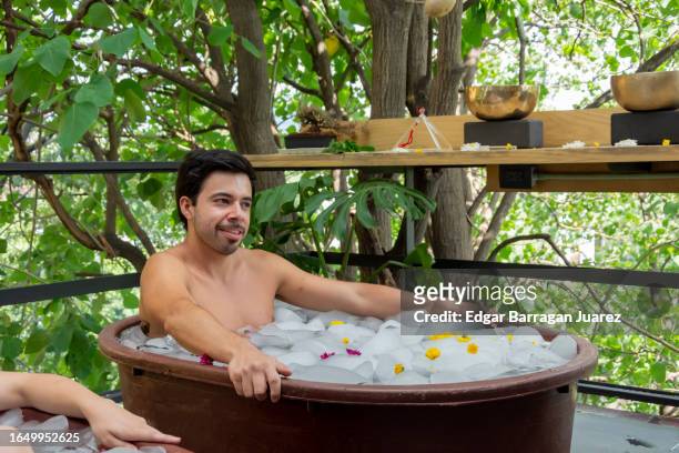 a man smiles as he practices cryotherapy inside an ice tub in a yoga class - bad breath stockfoto's en -beelden