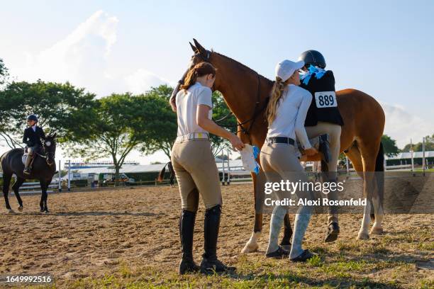 Trainers help a young equitation rider up while trying to mount her horse iduring the 48th Annual 2023 Hampton Classic Horse Show on August 27, 2023...