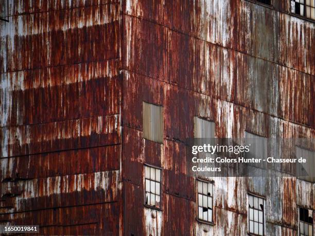 angled wall made of corrugated, rusty and weathered metal sheets with broken windows in montreal, quebec, canada - patina 個照片及圖片檔