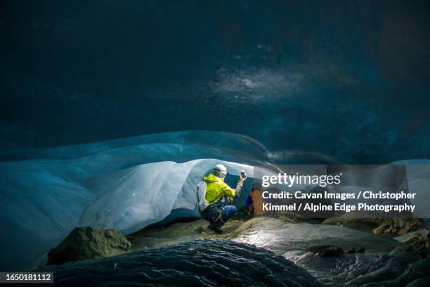rear view of two explorers in a low and narrow ice cave - crevasse fotografías e imágenes de stock