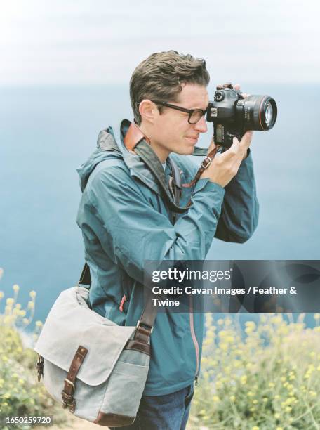 man in jacket taking picture of big sur coastline - water whorl grass stock pictures, royalty-free photos & images