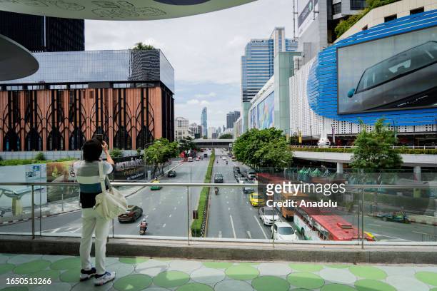 Person stops on the MBK Skywalk to take a picture of the King Power Mahanakhon Skyscraper as daily life continues in Bangkok, Thailand on August 30,...