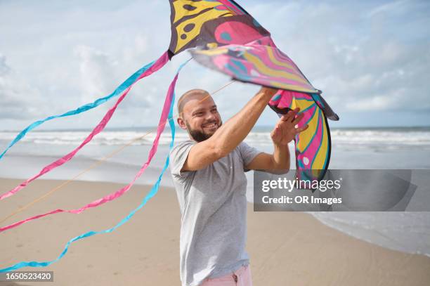 smiling man holding kite on the beach - indonesian kite stock pictures, royalty-free photos & images