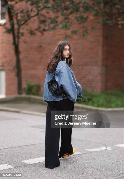 Carolina Tilgner seen wearing silver earrings and necklaces, black knit cropped top, blue oversized denim jacket, black wide leg suit pants, black...