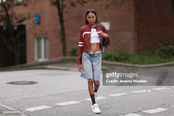 Wendy Brünings seen wearing gold earrings, black sunglasses, white cotton cropped top, iets frans red / white leather biker jacket, light blue denim...