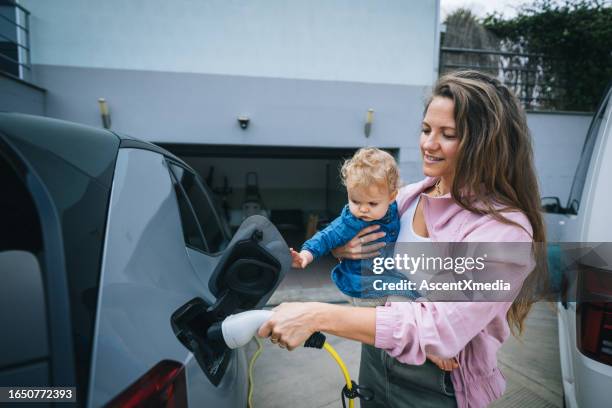 mutter und kind laden elektrofahrzeug auf - car home stock-fotos und bilder