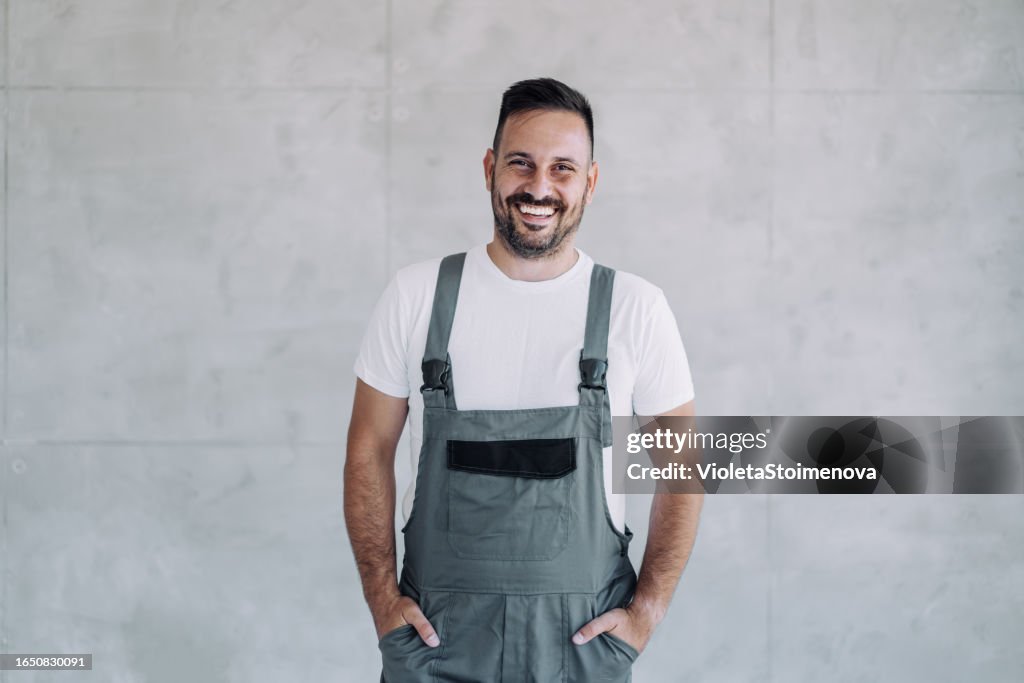 Junger männlicher Arbeiter in einer Gesamtuniform, der an seinem Arbeitsplatz posiert.