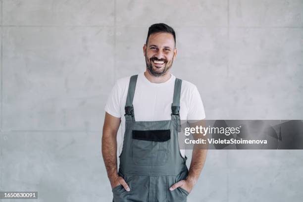 young male worker in an overall uniform posing at his workplace. - overalls stock pictures, royalty-free photos & images