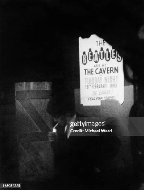 Man lighting a cigarette under a poster advertising a 19th February concert by The Beatles at the Cavern Club, Liverpool, 1st February 1963. The text...