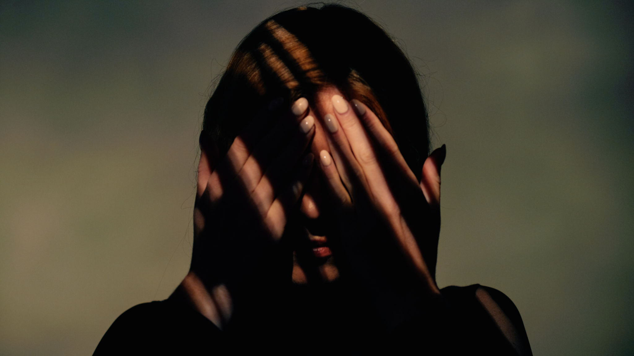 Woman covers her face with her hands. There are striped shadows on the face. Studio shot. Woman covers her face with her hands. There are striped shadows on the face. Studio shot.