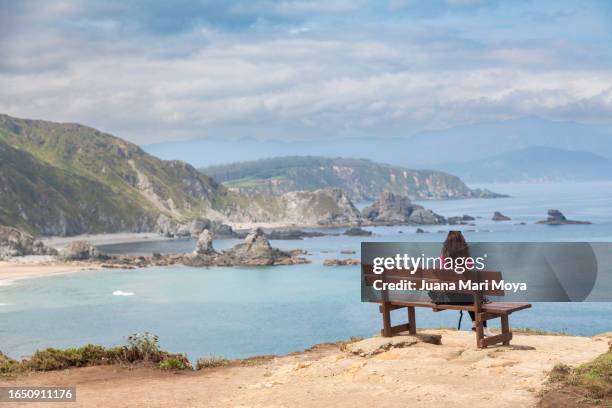 a woman tourist on the "the most beautiful bench in the world" at the famous loiba cliffs, in the village of loiba on the coast of the ortigueira estuary. - galicia fotografías e imágenes de stock