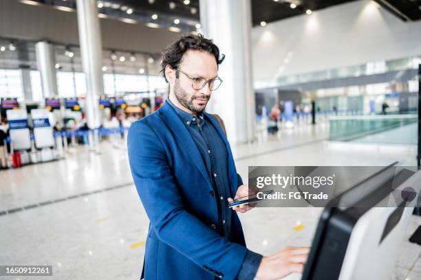 businessman using phone while checking in at airport self-service machine at airport - airport worker stock pictures, royalty-free photos & images