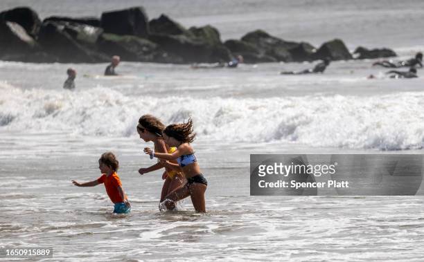 Children play in the surf as surfers ride waves at Rockaway Beach in New York as high surf from Hurricane Franklin delivers strong rip tides and...